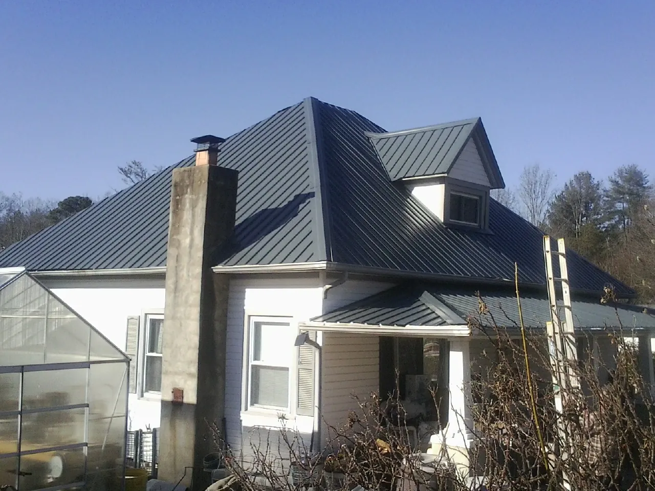 Dark blue standing seam metal roof on a white farmhouse with dormer — Slate & Tile Roof Repair by Roofing Brothers in Brownsdale