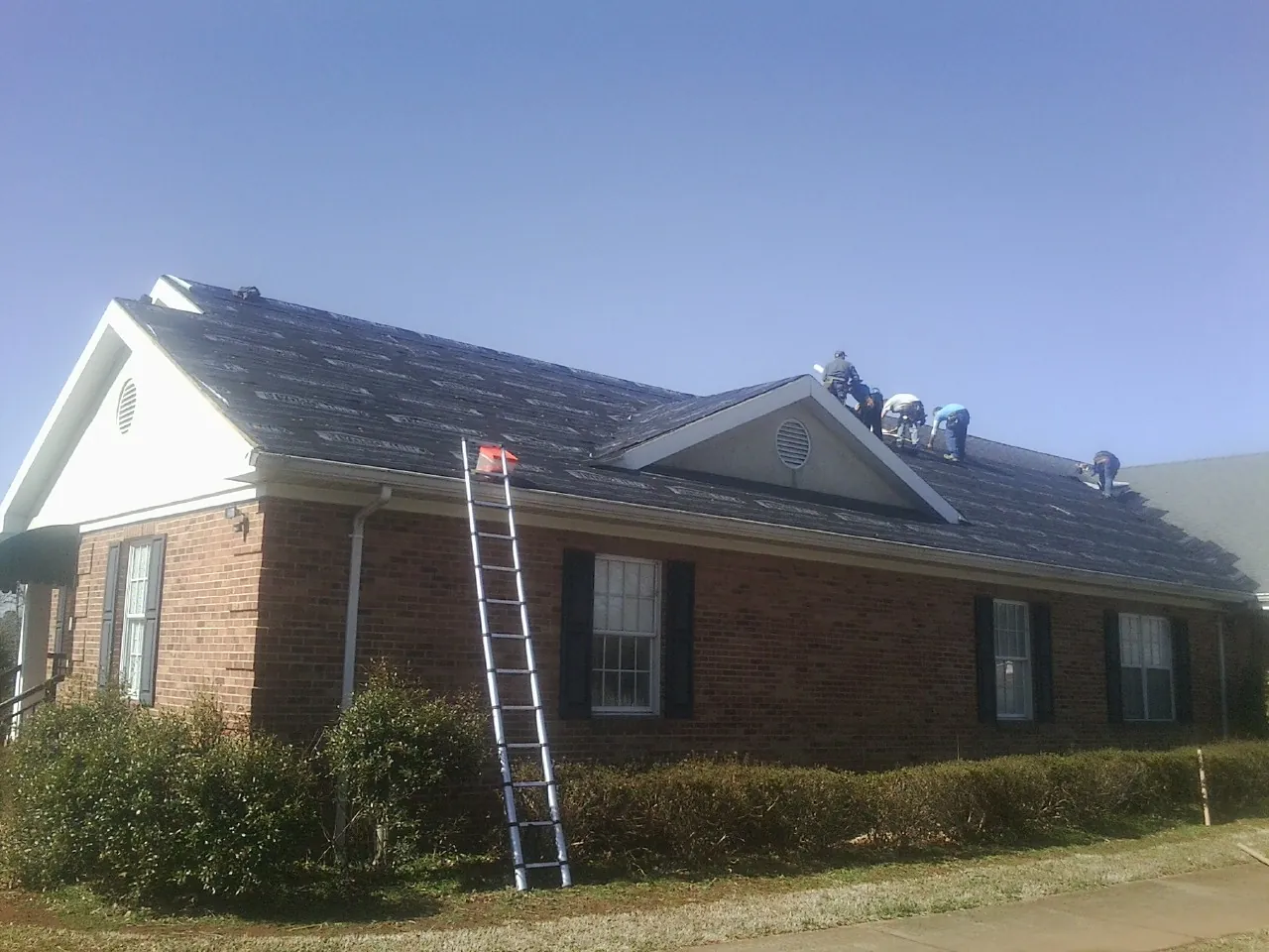 Crew tearing shingles off a brick ranch roof with a ladder set in Brownsdale