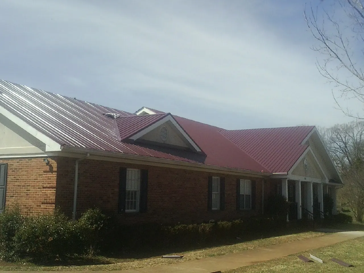 Red metal roof with gabled entries on a long brick building, from a Hail Damage Roof Repair job in Brownsdale