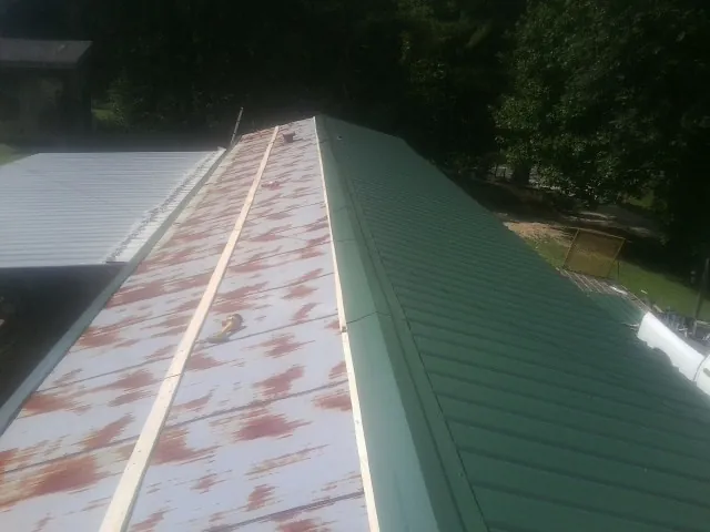 Old rusted panels beside newly installed green metal roofing — Wind Damage Roof Repair by Roofing Brothers in Brownsdale