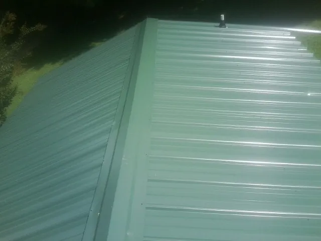 New green metal panels meeting at the ridge of a roof — Flat Roof Repair work by our crew in Brownsdale