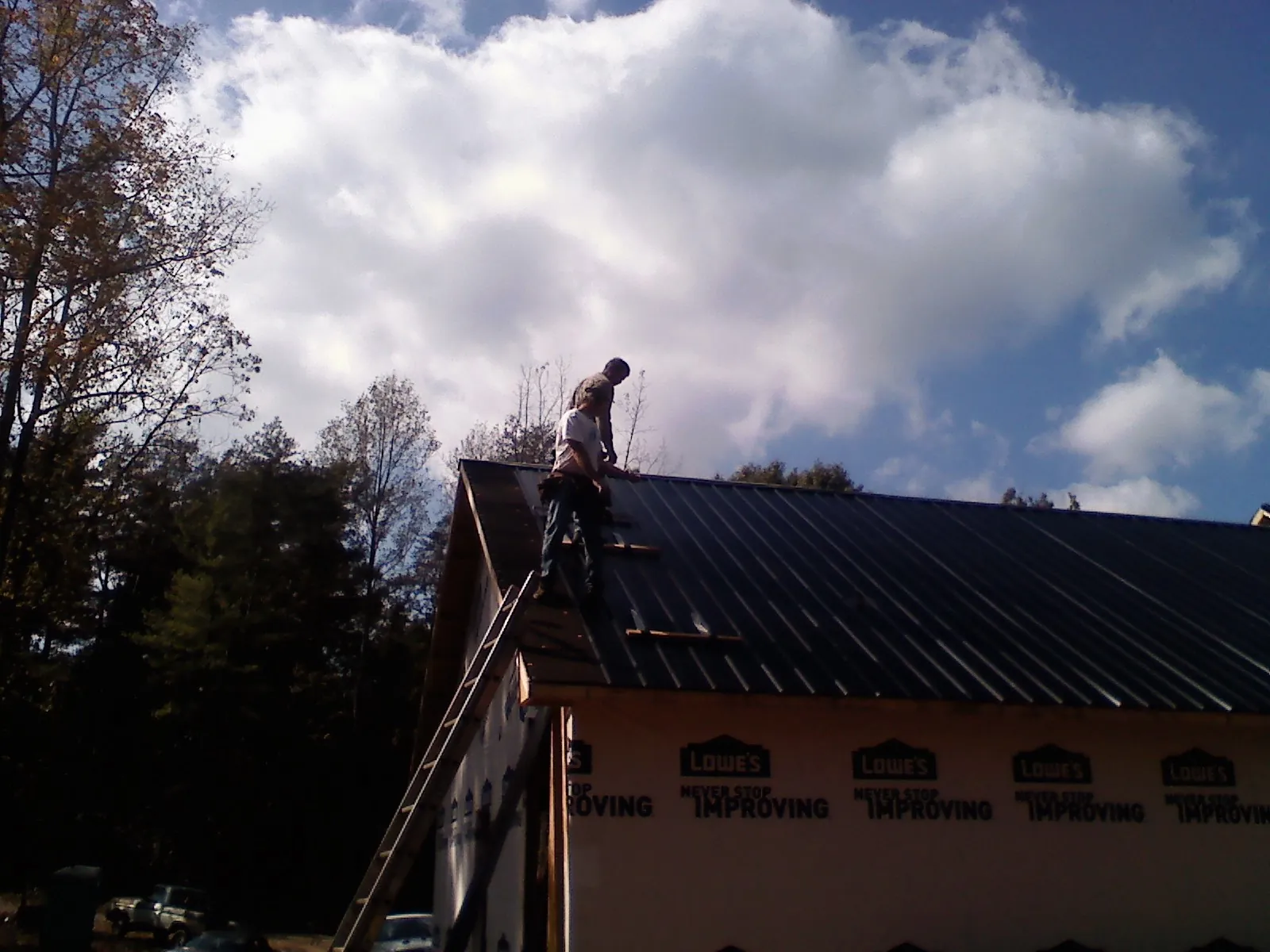 Roofer fastening dark metal panels high against a cloudy sky, from a Roof Inspection job in Brownsdale