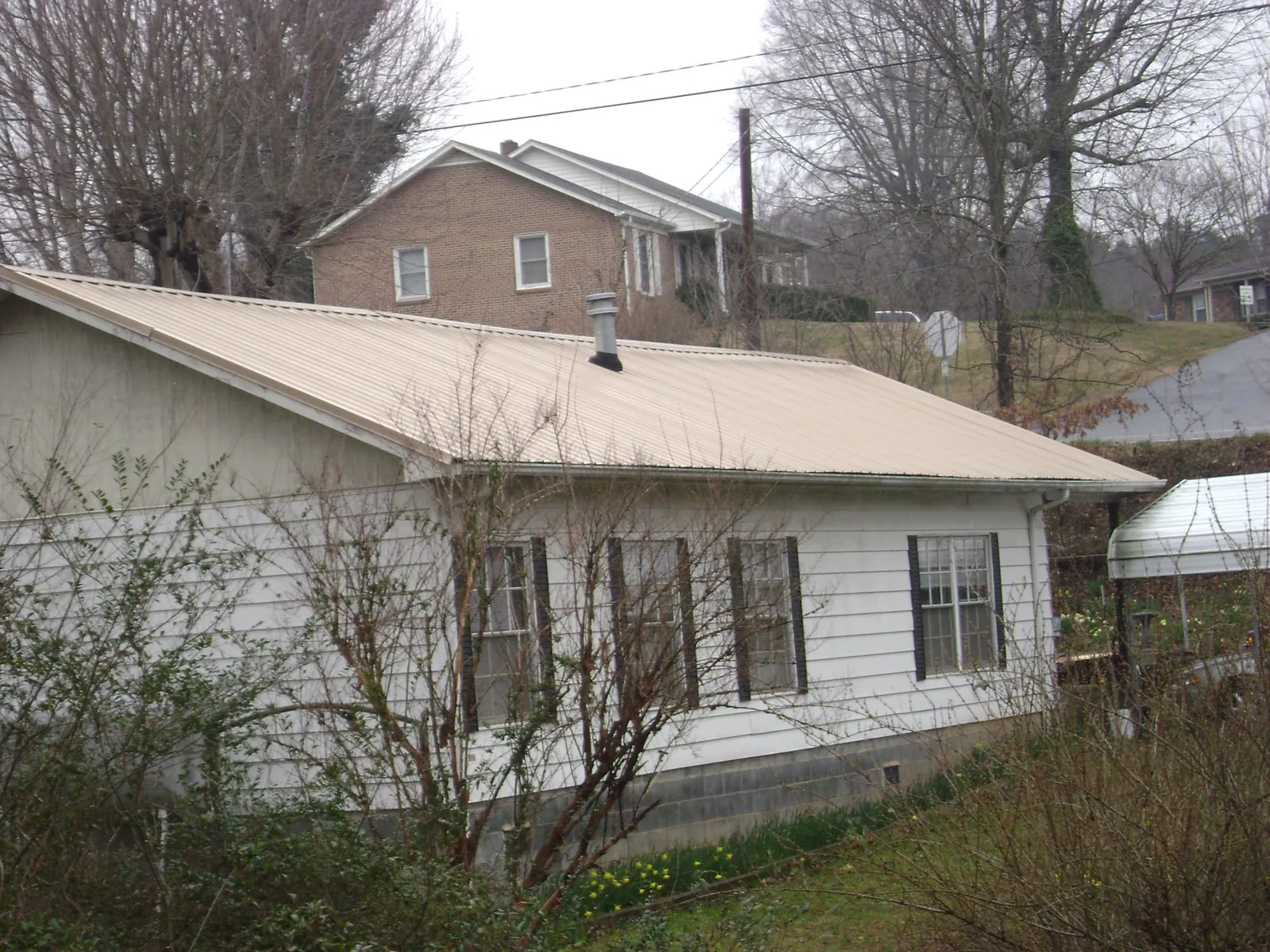 Tan metal roof on a white sided house set into a hillside — Commercial Roofing by Roofing Brothers in Brownsdale