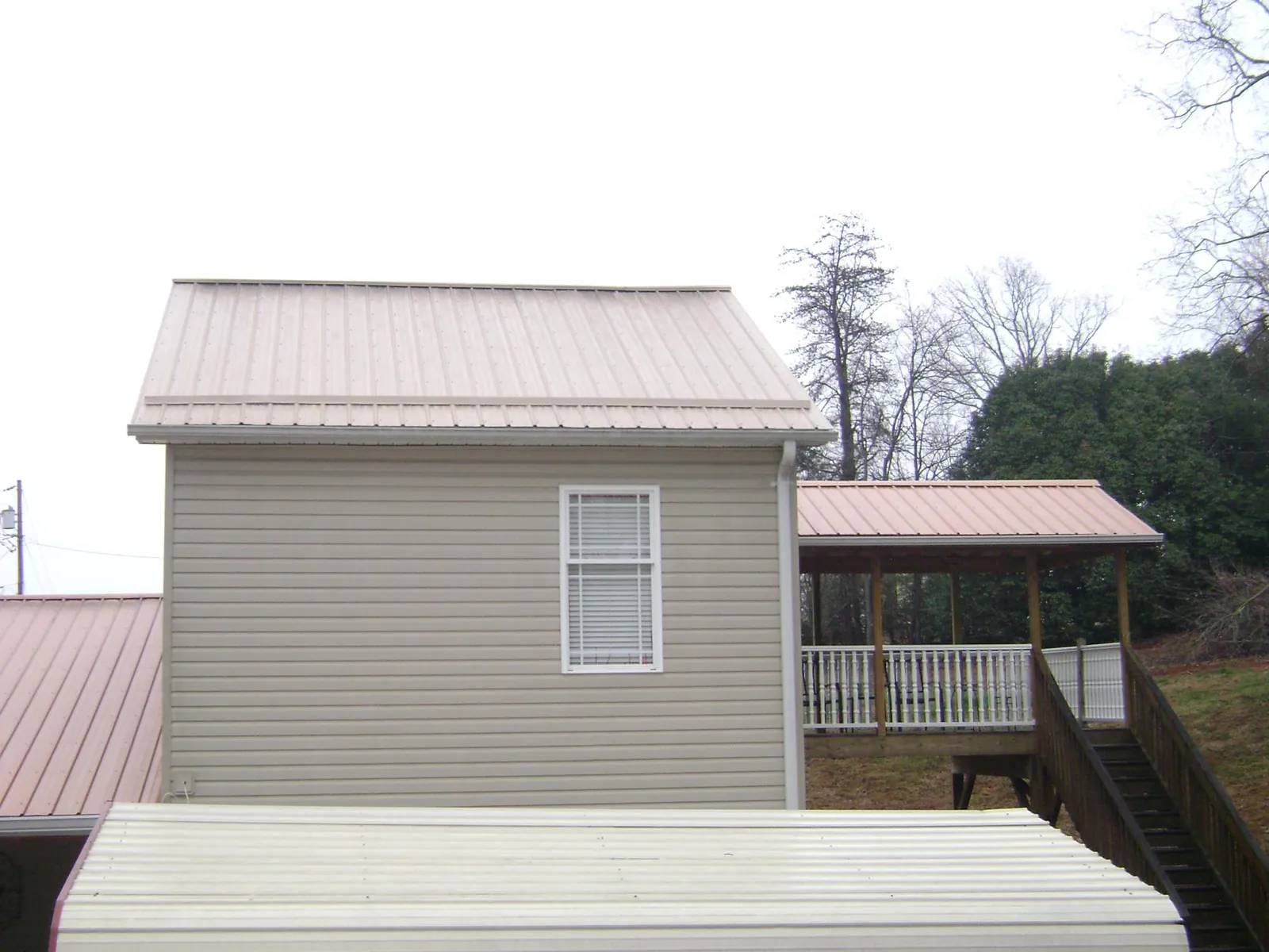 Tan metal roofs on a two story addition and attached porch, from a Roof Replacement job in Brownsdale
